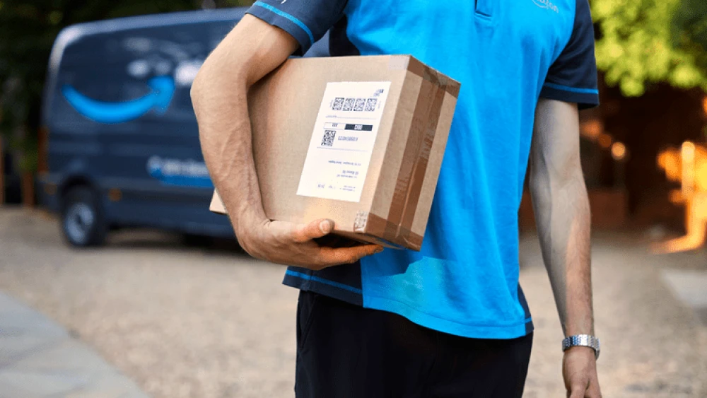 The torso of an Amazon delivery driver holding a package under one arm