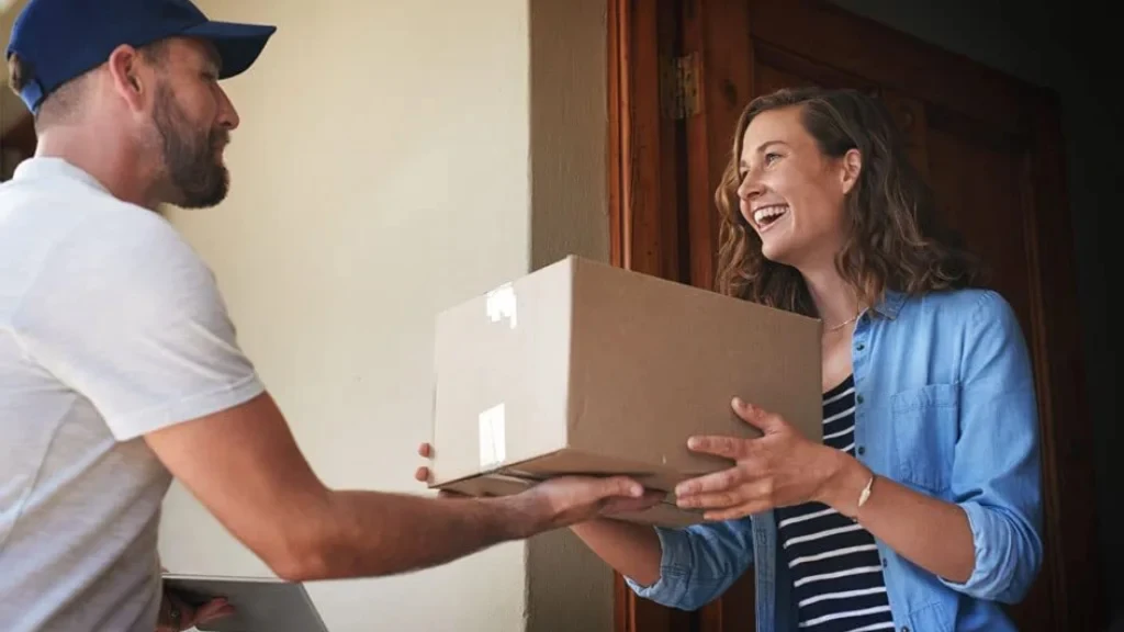 Package delivery handoff at front door between person in white shirt and person in blue denim shirt