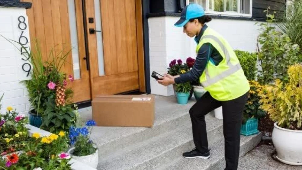 A woman in a safety vest and Amazon hat delivers a package