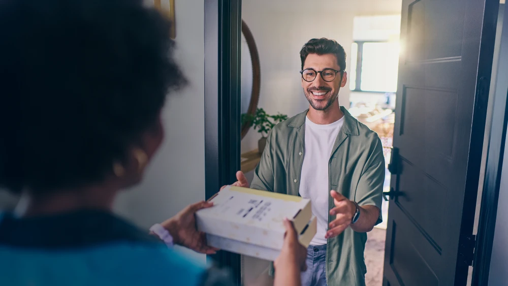 Package delivery at front door, person in glasses and casual attire greeting delivery worker with a friendly smile