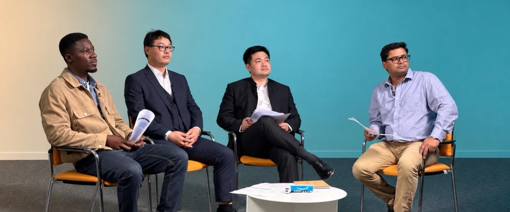 Vier M&auml;nner sitzen w&auml;hrend einer Podiumsdiskussion auf St&uuml;hlen, vor ihnen ein kleiner wei&szlig;er Tisch mit Papieren.