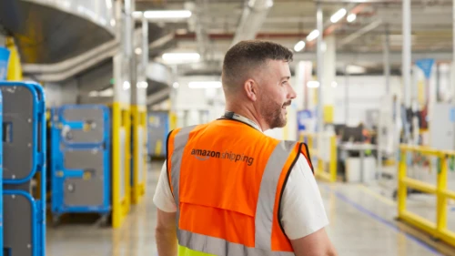 A man in an orange Amazon safety vest walking in a warehouse.